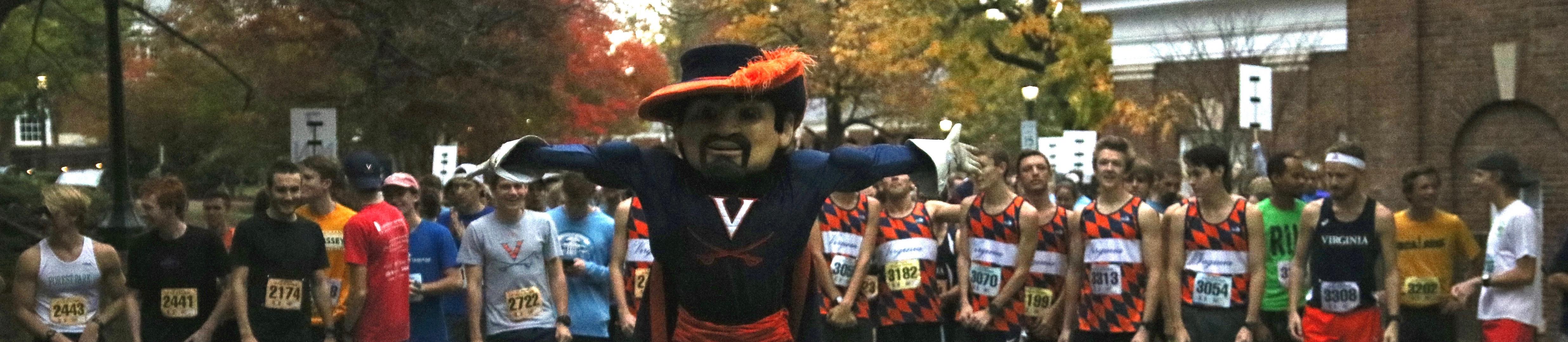 The UVA Cavaliers mascot stands in front of the starting line of the 4th Year 5k, runners are lined up behind him.