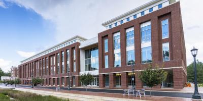 A four-story brick building with windows, blue sky and clouds visible.