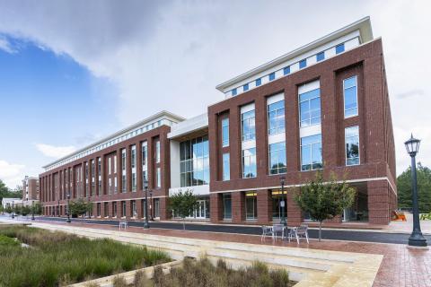 A four-story brick building with windows, blue sky and clouds visible.