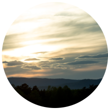 A circular photo of the sun setting over the mountains