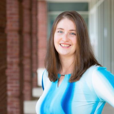 Martina smiling and wearing a blue shirt while standing outside of the Student Health and Wellness building