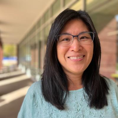 Sonya smiling while wearing glasses and a blue top outside of the Student Health and Wellness Building