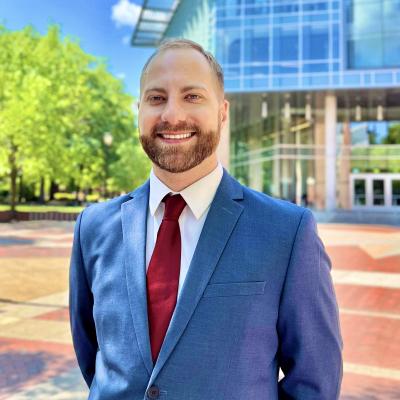 Aaron Keen wearing a blue jacket, white shirt, and red tie